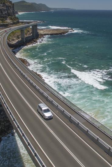 Aerial of a car taking the scenic route over Sea Cliff Bridge, Clifton